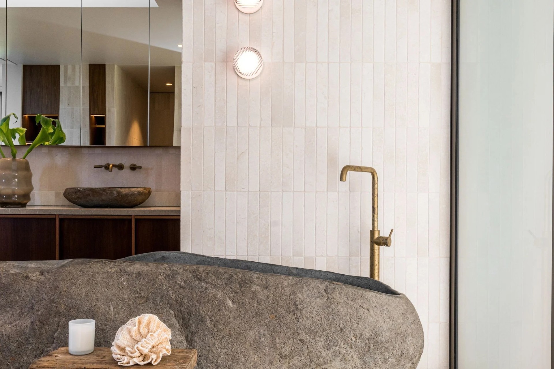 Luxury bathroom with a natural stone bath, aged brass floor-mounted tapware, vertical stack tiles and walnut vanity