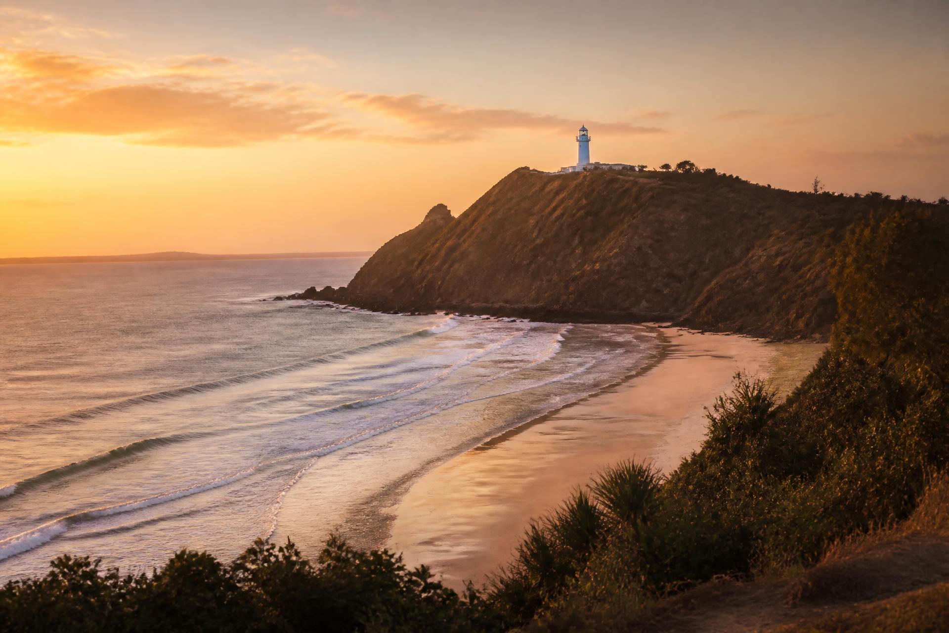 Byron Bay lighthouse on the headland at warm dusk, curving beach below