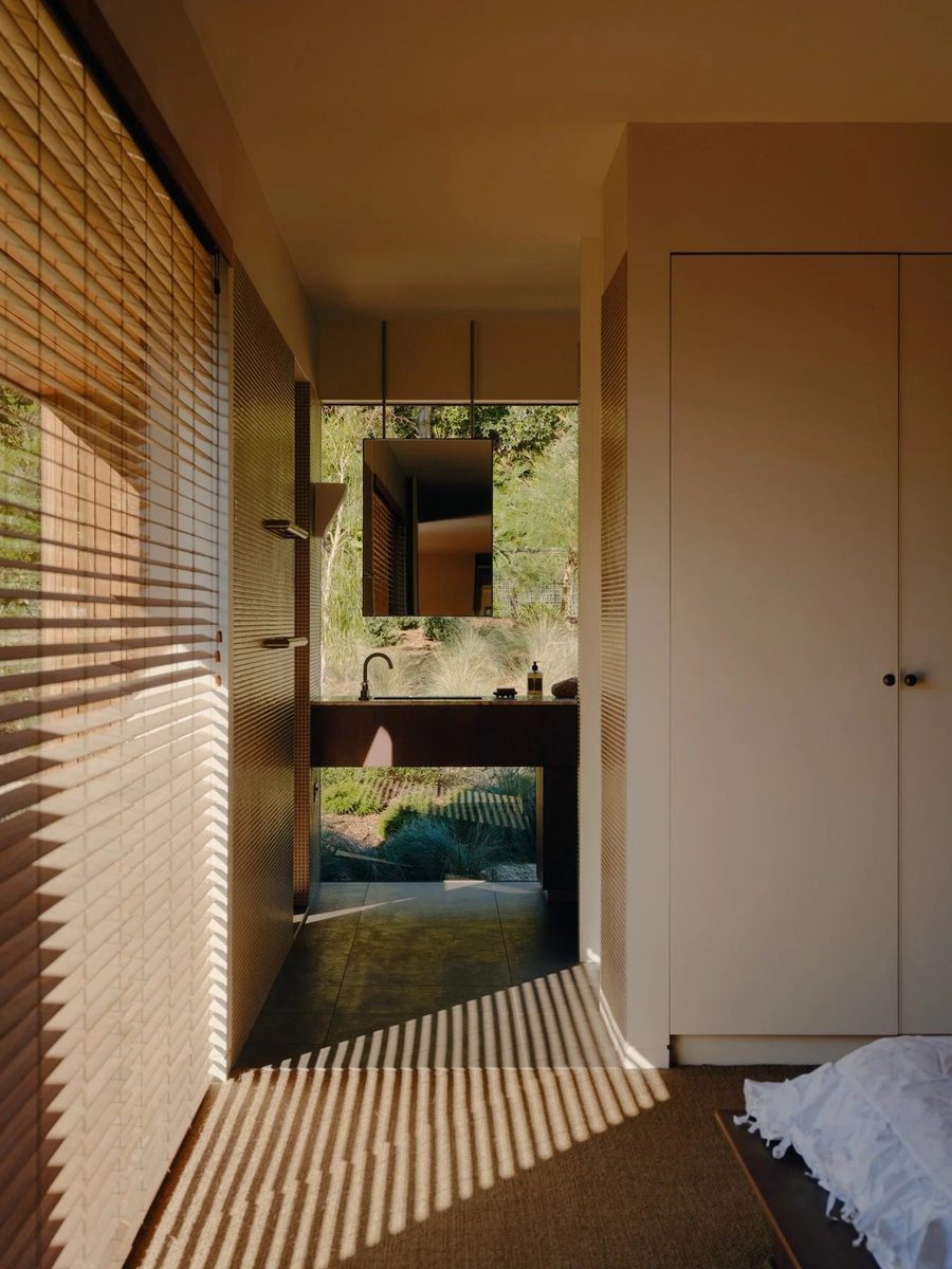 Field House bedroom looking through bamboo blinds to an outdoor stone basin nestled in native grasses