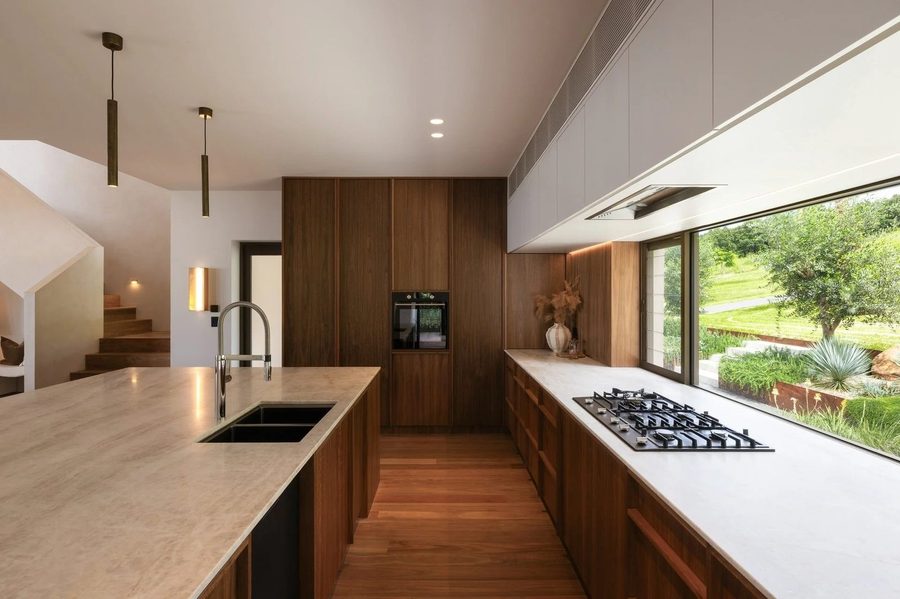 Leadbeatters walnut galley kitchen with stone benchtop, chrome mixer, gas cooktop and picture window overlooking green hills