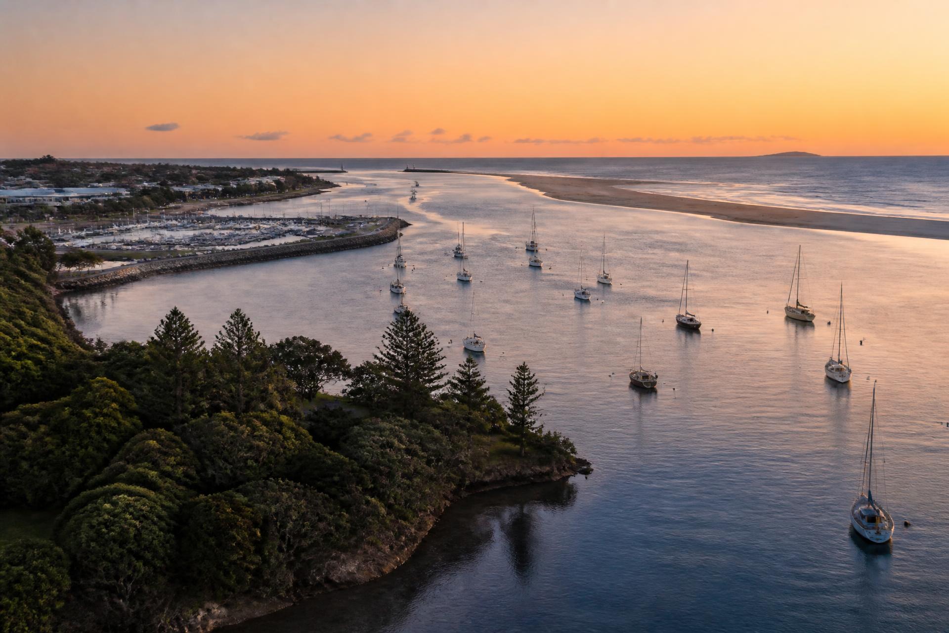 Aerial view of Ballina Richmond River mouth at warm dusk, moored boats and headland