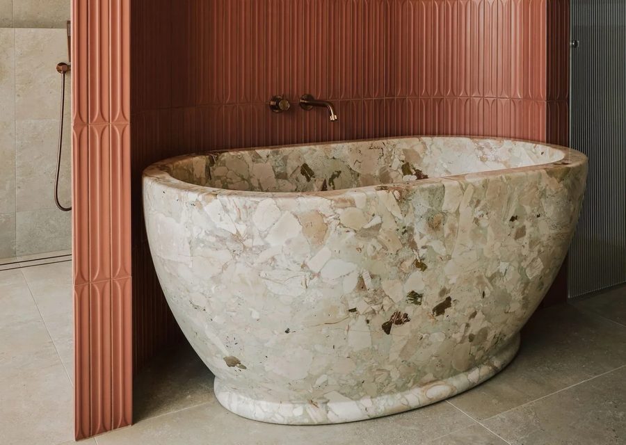 Freestanding rough-cut marble bath against fluted terracotta tiles with aged brass wall-mounted tapware