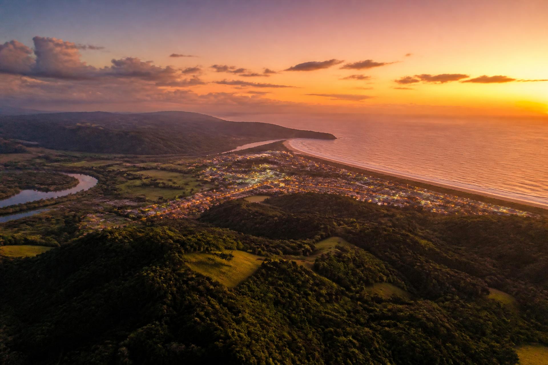 Aerial view of the Northern Rivers NSW coastline at warm dusk, hinterland green rolling into the ocean